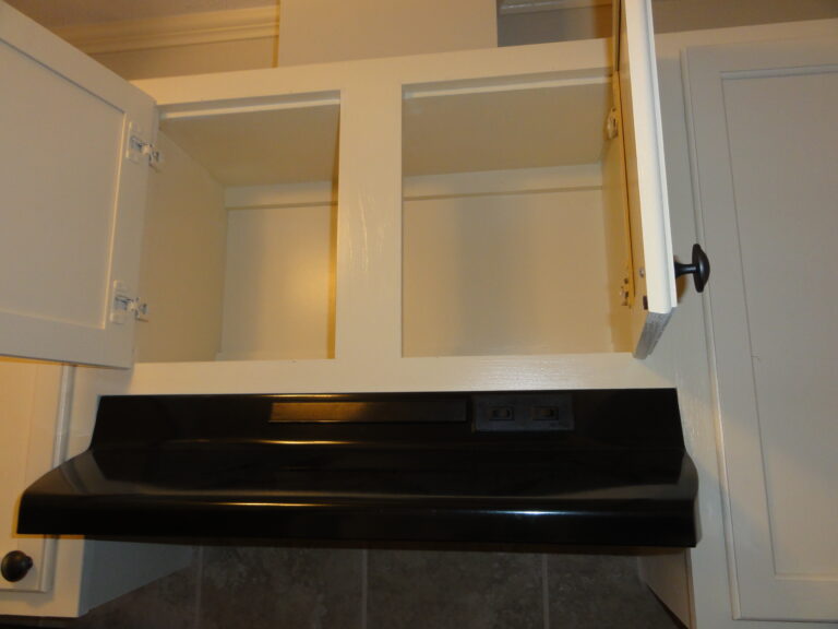 Open white kitchen cabinet with empty shelves above a black stove.