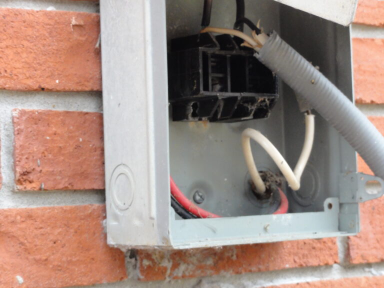 Exposed electrical wires inside a metal box on a brick wall.