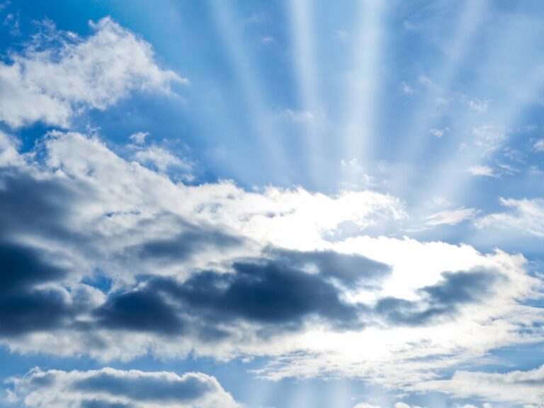 Sunlight beams radiate through scattered clouds in a blue sky.