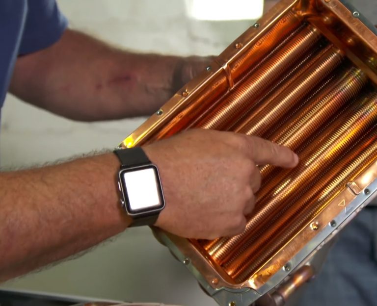 Person pointing at a shiny copper pipe assembly.