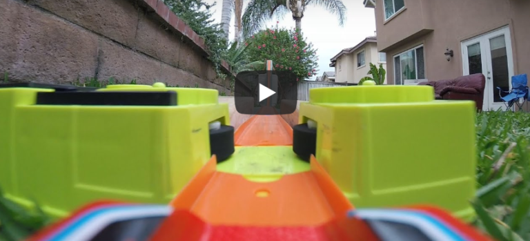 Close-up of a toy car track with green cars and palm trees in the background.
